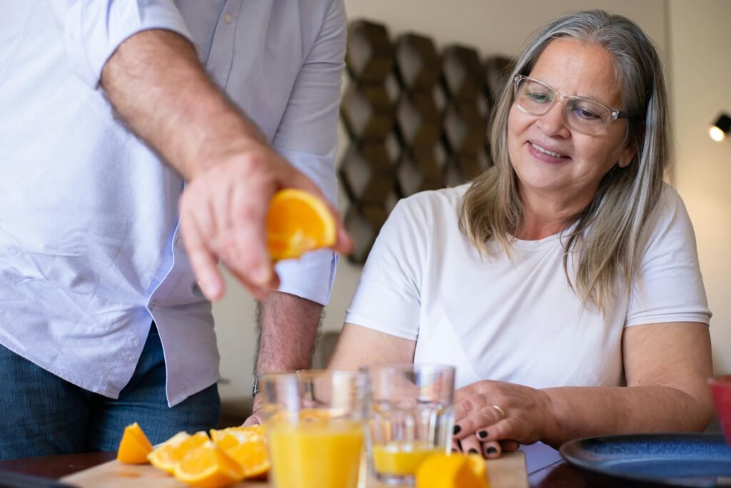 A senior woman smiles while an orange is squeezed for fresh juice at home.